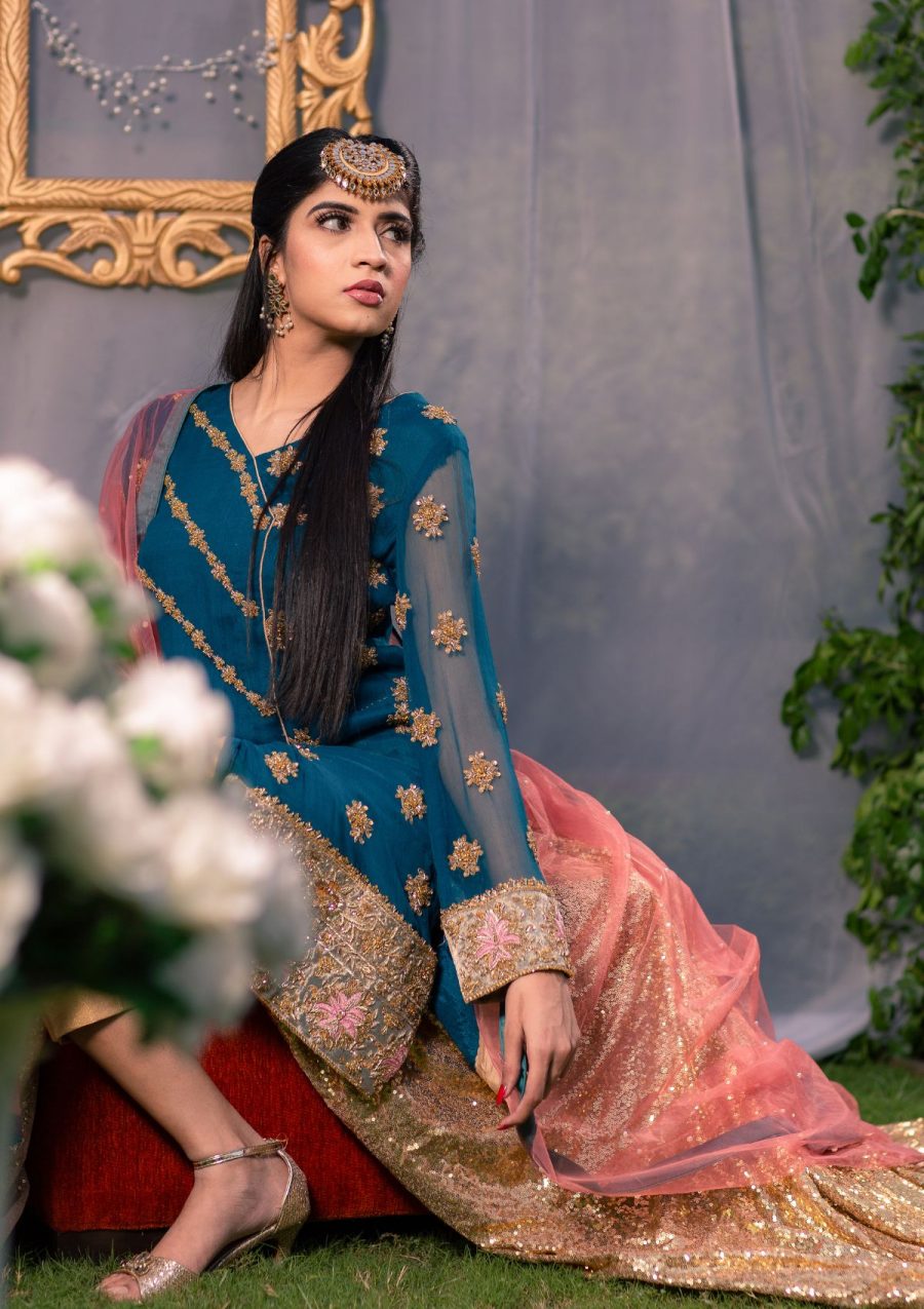 Teal green short gold embellished shirt with angrakha style cutline on chiffon fabric paired with gold pants and contrasting net dopata with a bit spray on it.