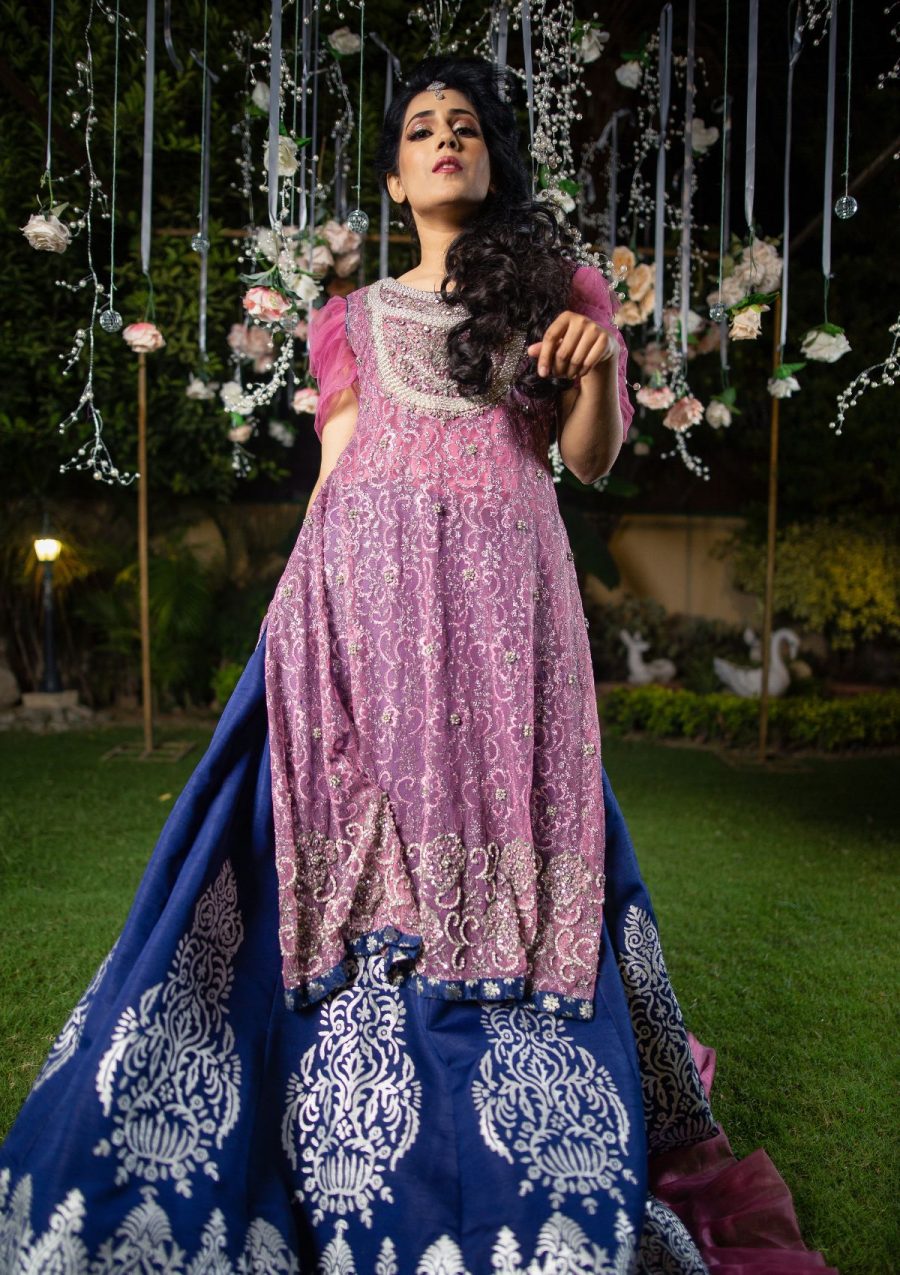 Long net shimmer shirt with silver pearls and stones work on neckline and hem with draped sleeves of chiffon fabric and finishing of contrasting blue jamawar fabric use on it also full flared navy blue raw silk panelled lehnga with silver block printed work and finishings of organza pleated border makes the look amazing.