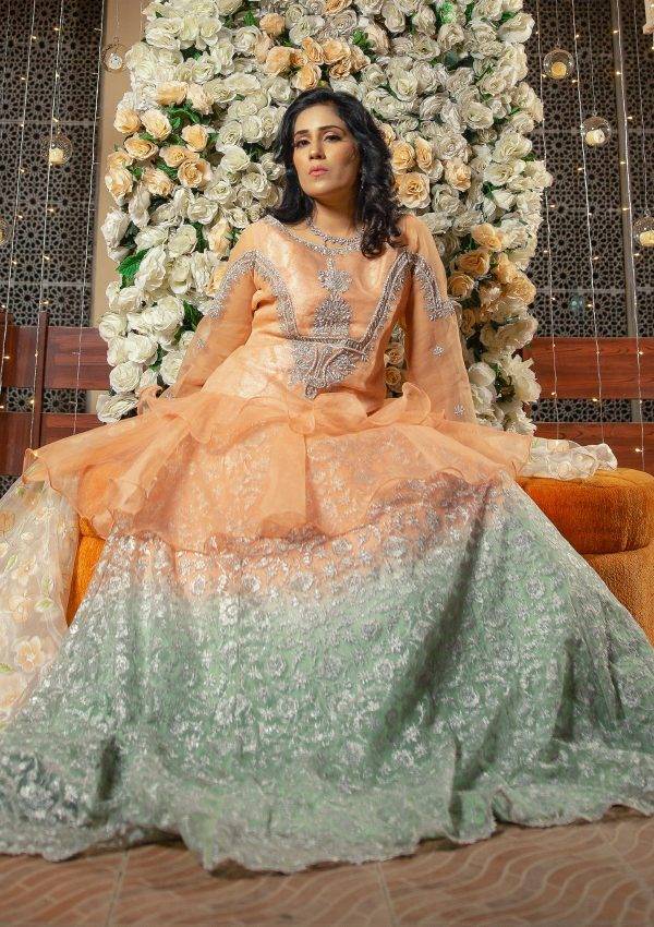 Peachy stylish flared short length peplum in organza fabric with silver hand work of naqshi, dapka, stones on it paired with peach and green shaded tye and dye fully embroidered net lehnga with silver tilla work on it also having printed organza dopata makes the look perfect for the wedding season.