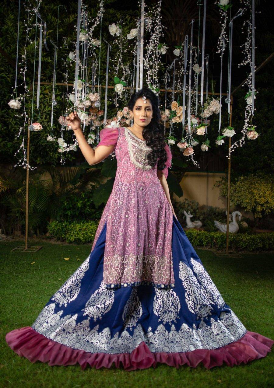 Long net shimmer shirt with silver pearls and stones work on neckline and hem with draped sleeves of chiffon fabric and finishing of contrasting blue jamawar fabric use on it also full flared navy blue raw silk panelled lehnga with silver block printed work and finishings of organza pleated border makes the look amazing.